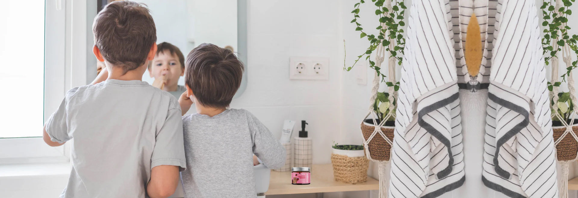 Two children looking at themselves in a mirror with a bathrobe hanging on a rack in the background.